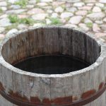 Cuve en bois ouverte remplie d'eau de pluie sur des pavés